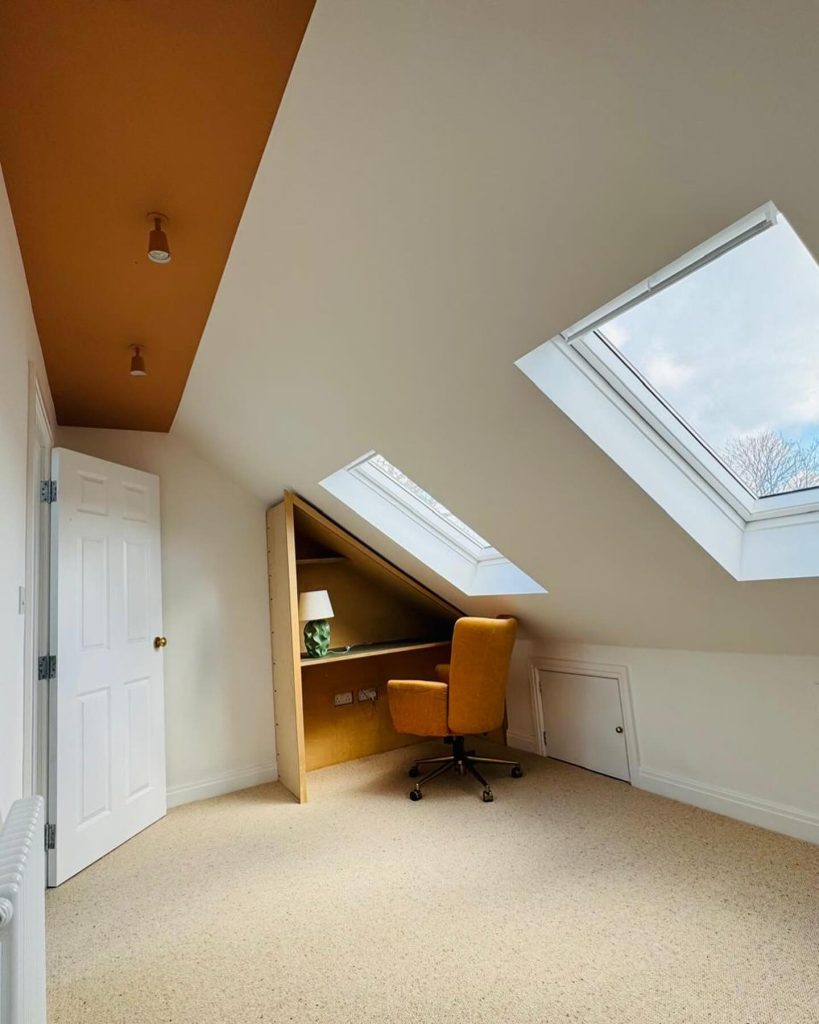 Loft conversion with two skylights, built-in desk, mustard chair, and modern ceiling feature by J2 Build.”