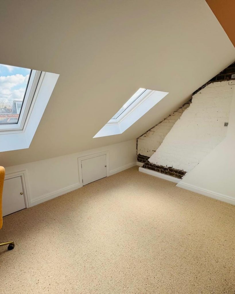 Loft conversion with two skylights, exposed brick feature wall, storage doors, and neutral carpet flooring by J2 Build