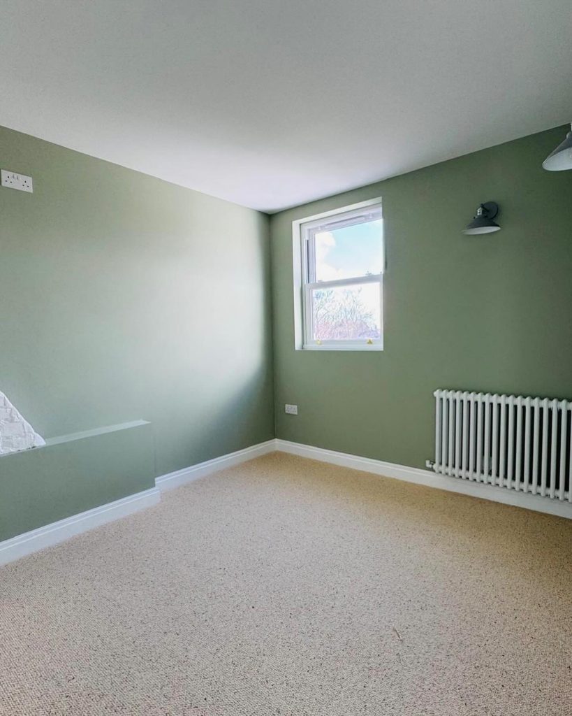 Loft conversion bedroom with green walls, new radiator, and fresh carpeting completed by J2 Build.