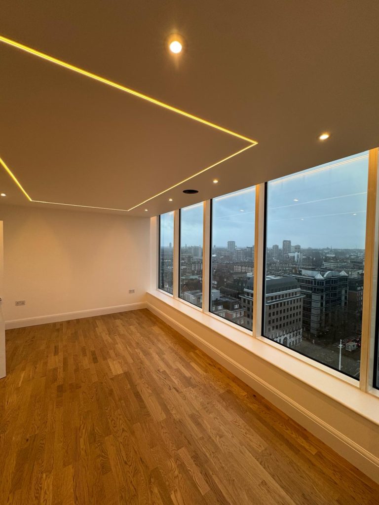 LED strip lighting and recessed spotlights installed in a modern room with full-height windows overlooking the city.