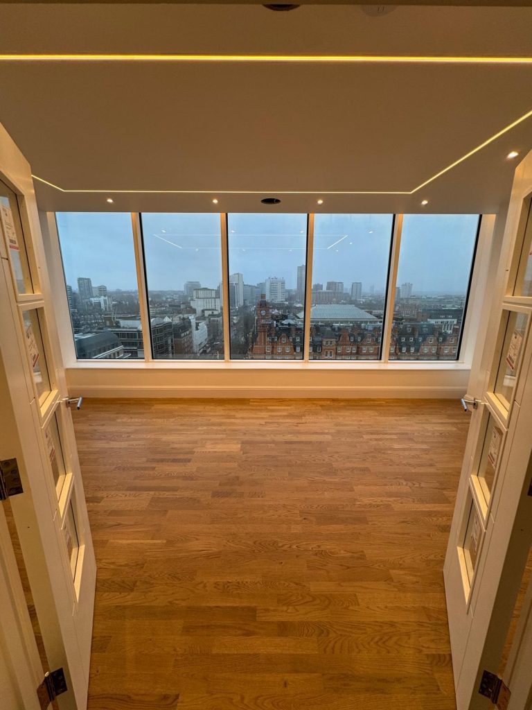 Modern lighting installation with LED strip lighting, recessed spotlights, and full-height glazed windows overlooking the city.